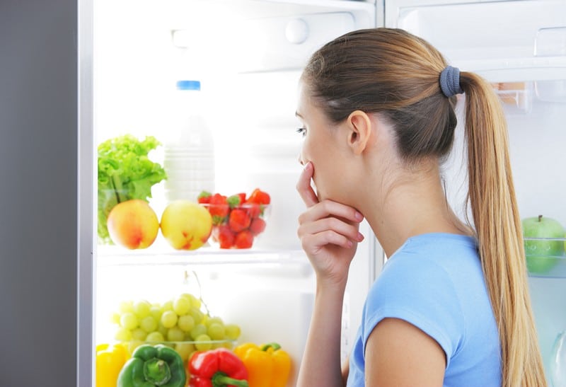 Young woman craving food choosing near refrigerator